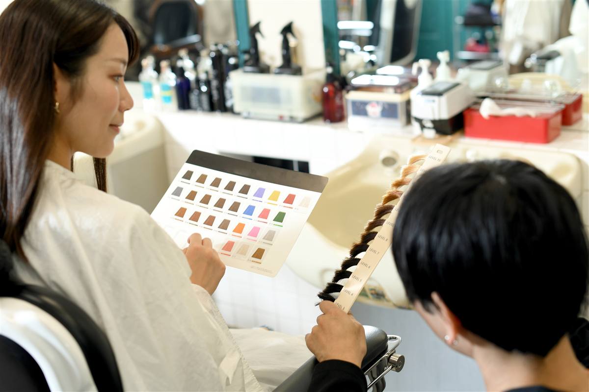 美容室で、カラーチャートを見ながら髪の色を選ぶお客様と美容師