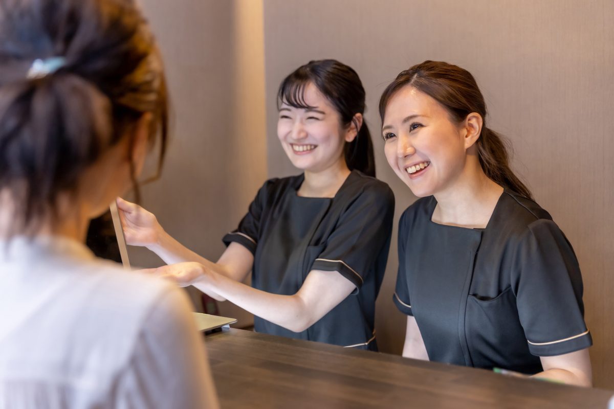 美容サロンの受付で、カウンター越しにお客様を迎える2人のスタッフ
