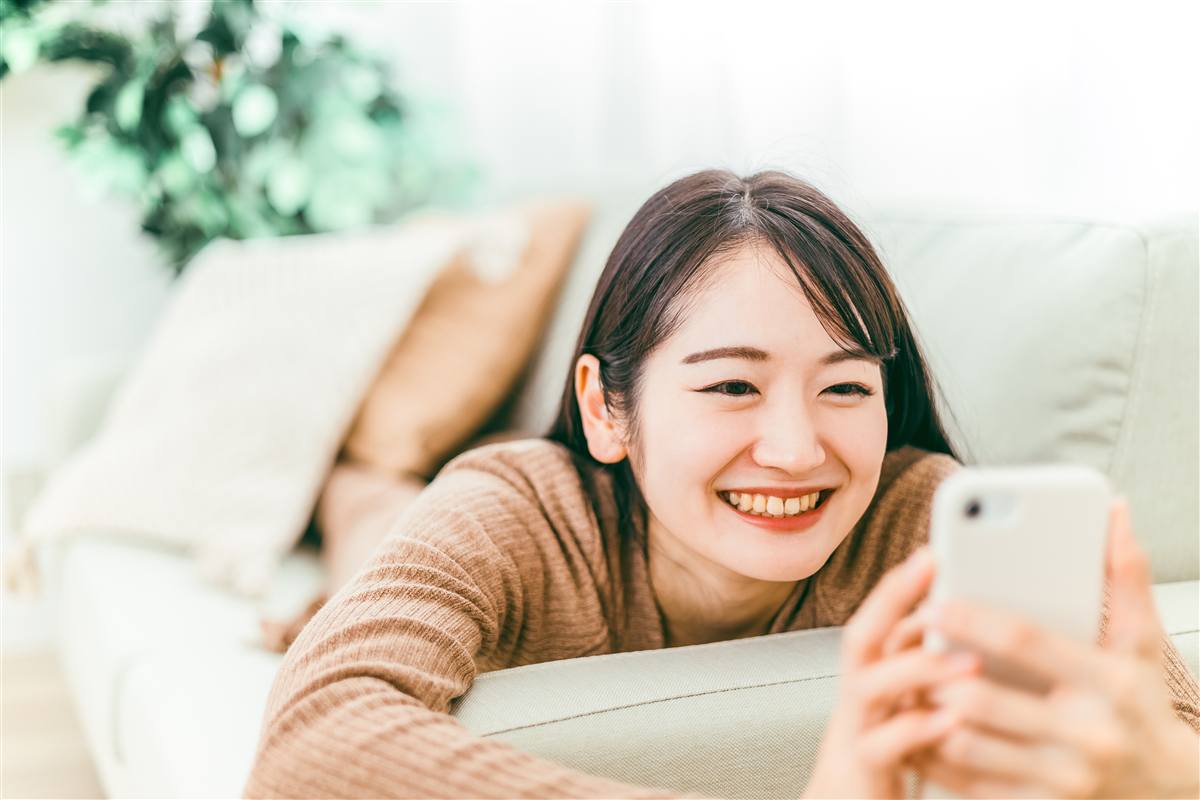 ソファでスマートフォンを見て笑う女性