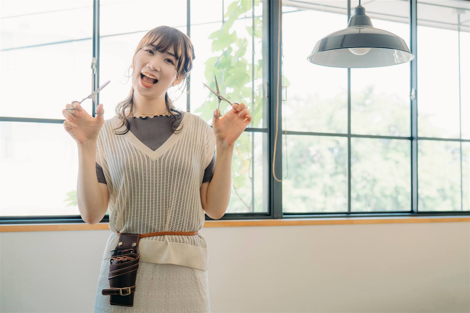 窓際の明るい美容室で、はさみを手に笑う美容師
